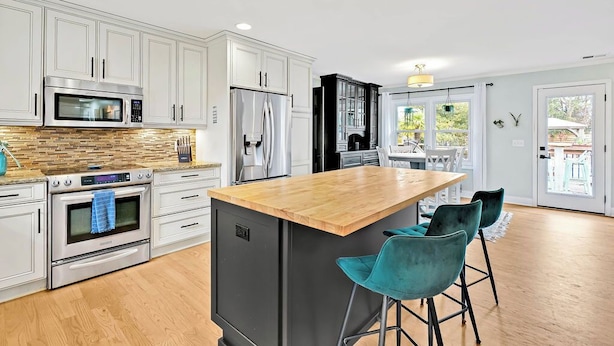Una cocina moderna con gabinetes blancos, electrodomésticos de acero inoxidable, una isla de madera y taburetes de color turquesa.