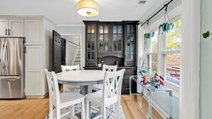 Una cocina moderna con armarios blancos, un refrigerador de acero inoxidable, una mesa redonda de comedor con sillas blancas y una lámpara colgante.