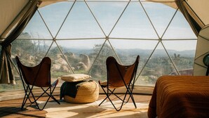 A tent with a view of the landscape, two folding chairs, a small round table, and a bed. - A Cozy Fireside Glamping Escape with Ridge Views (Fallbrook)
