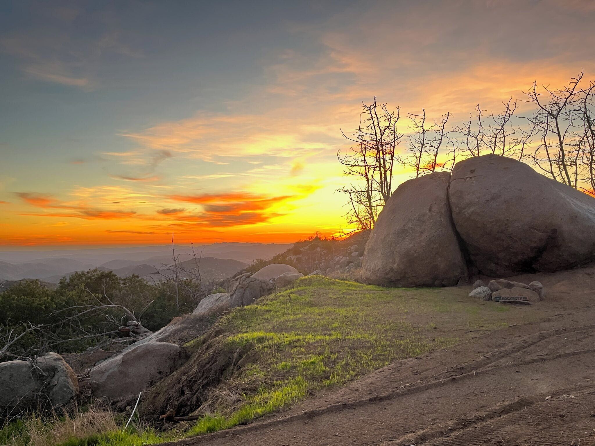 A natural landscape with large boulders, a grassy area, and a clear sky during sunset.