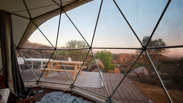 Une pièce en forme de dôme géodésique dotée d’une terrasse en bois, d’une table de pique-nique et offrant une vue sur le paysage environnant.