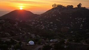 Une structure en forme de dôme, située dans un environnement naturel, avec un coucher de soleil en arrière-plan.
