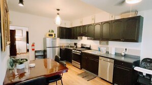Una cocina con armarios oscuros, electrodomésticos de acero inoxidable, una mesa de comedor de madera y un ventilador de techo.