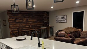 Una cocina moderna con una isla grande, armarios blancos y revestimiento de pared estilo campestre.