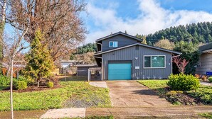 A two-story house with a blue garage door, surrounded by a well-maintained lawn and a small pond. - Spacious yet cozy 3-BR home in lovely SE Eugene near University of Oregon (Eugene)