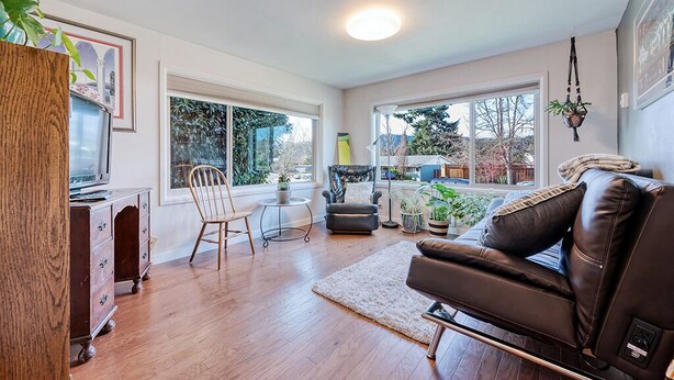 A living room with a wooden floor, a brown leather sofa, a wooden cabinet, a television, and a large window with a view of trees. - Spacious yet cozy 3-BR home in lovely SE Eugene near University of Oregon (Eugene)