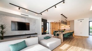 Een moderne woonkamer met een grote flatscreen-televisie, een open haard en een eethoek, met een keuken op de achtergrond.