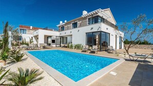 Een modern herenhuis met zwembad, terras en een stenen muur.