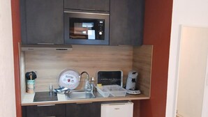 A compact kitchen with dark cabinets, a microwave, a sink, and a small refrigerator. - The groundhog (La Bresse)