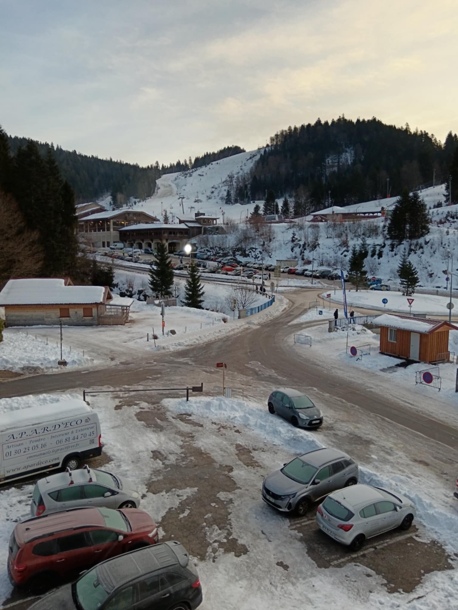 A parking area with several cars and a building with snow-covered roofs.