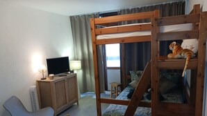A room with a bunk bed, a desk with a computer, a chair, a table with a candle, and a window with curtains. - The groundhog (La Bresse)