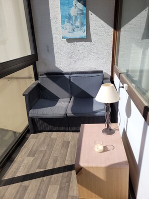 A corner of a room with a dark-colored sofa, a small table with a lamp, and a wall with a picture. - The groundhog (La Bresse)