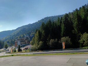 A parking lot with a road leading to a building complex surrounded by dense forest and hills. - The groundhog (La Bresse)