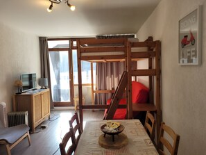 A room with bunk beds, a television, a table with a placemat, and a radiator. - The groundhog (La Bresse)