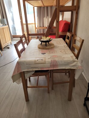 A dining table with a checkered tablecloth, surrounded by wooden chairs, in a room with a sloped ceiling and a window with curtains. - The groundhog (La Bresse)