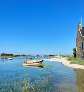 A clear waterfront scene with boats, a stone building, and a sandy beach.
