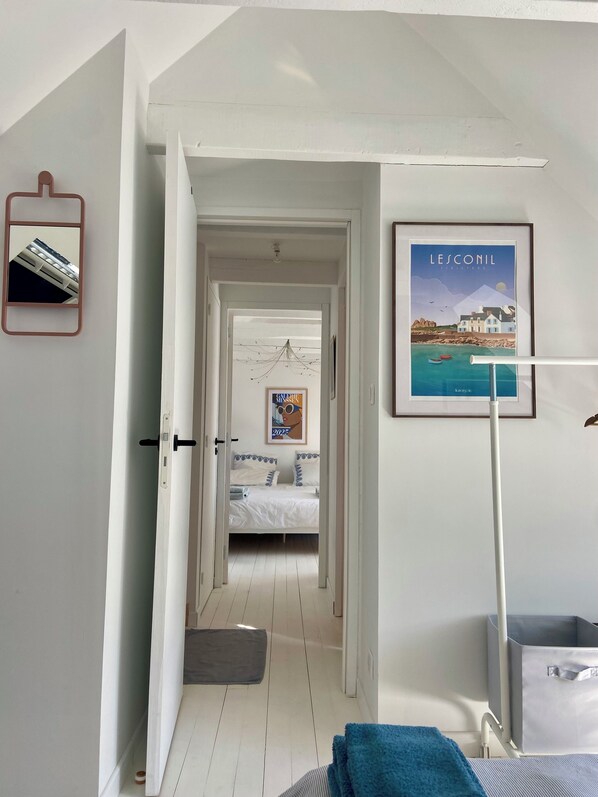 A hotel room with a bed, a bathroom with a towel, a framed picture on the wall, and a door leading to another room.