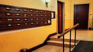Un couloir avec un distributeur de courrier en bois, un escalier doté d’une rampe et une porte visible au fond.