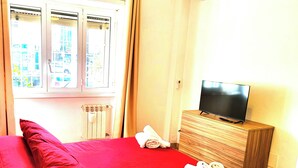 Une chambre d’hôtel avec un lit, un téléviseur posé sur une commode en bois et une fenêtre avec des rideaux.