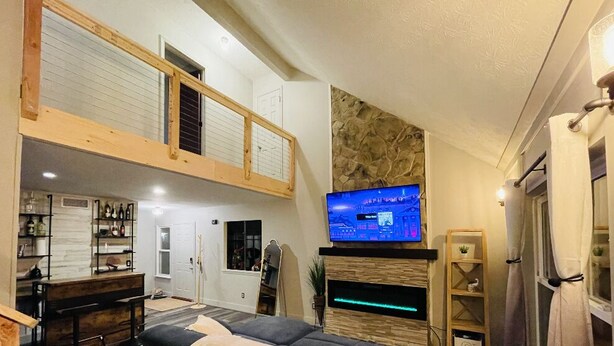 Ein geräumiges Wohnzimmer mit hoher Decke, einem an einer Steinwand befestigten Fernseher, einer Holzbank und einem Kamin.