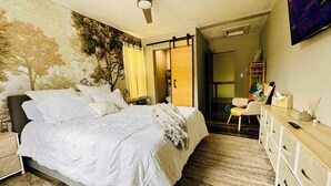 Ein Schlafzimmer mit einem Bett, einem Nachttisch, einer Kommode, einem Deckenventilator und einem an der Wand montierten Fernseher.