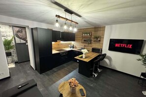 Cocina moderna con armarios negros, una isla de madera y un televisor empotrado que muestra 'NETFLIX'.