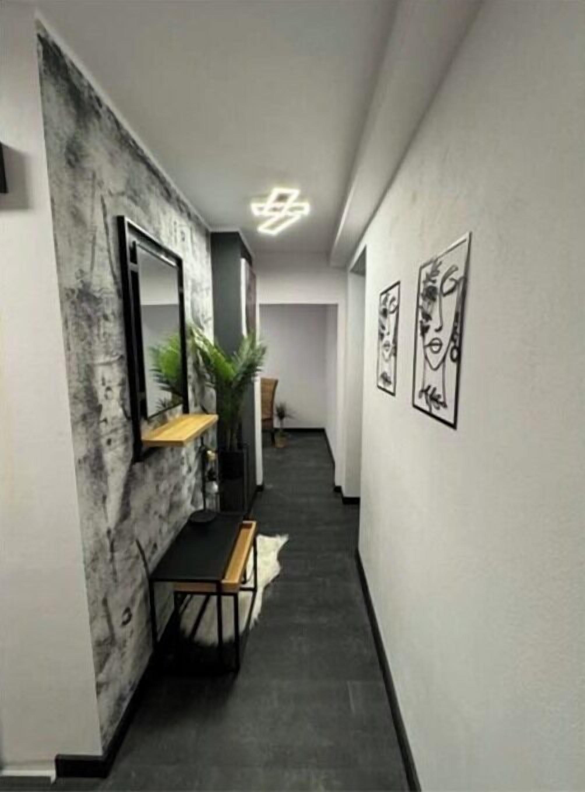 Een hal met een modern design, met een donkere vloer, een houten bankje, een wandspiegel en ingelijste kunstwerken.