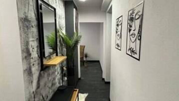 Een hal met een modern design, met een donkere vloer, een houten bankje, een wandspiegel en ingelijste kunstwerken.