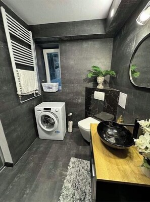 Un baño pequeño con lavadora, inodoro y lavamanos de color negro.