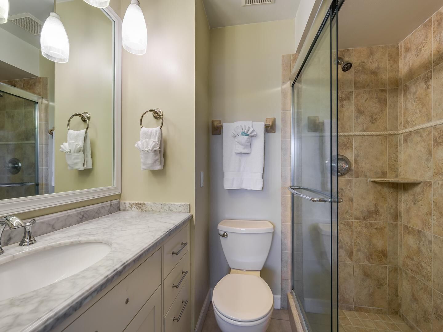 A bathroom with a marble sink, a toilet, and a glass shower enclosure.