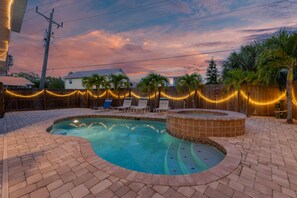 A backyard with a swimming pool, a hot tub, and a wooden fence adorned with string lights. - Island Charm (Fort Myers Beach)