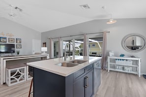 A modern kitchen with a central island, a dining area with a bench, and a view through a glass door to an outdoor space.