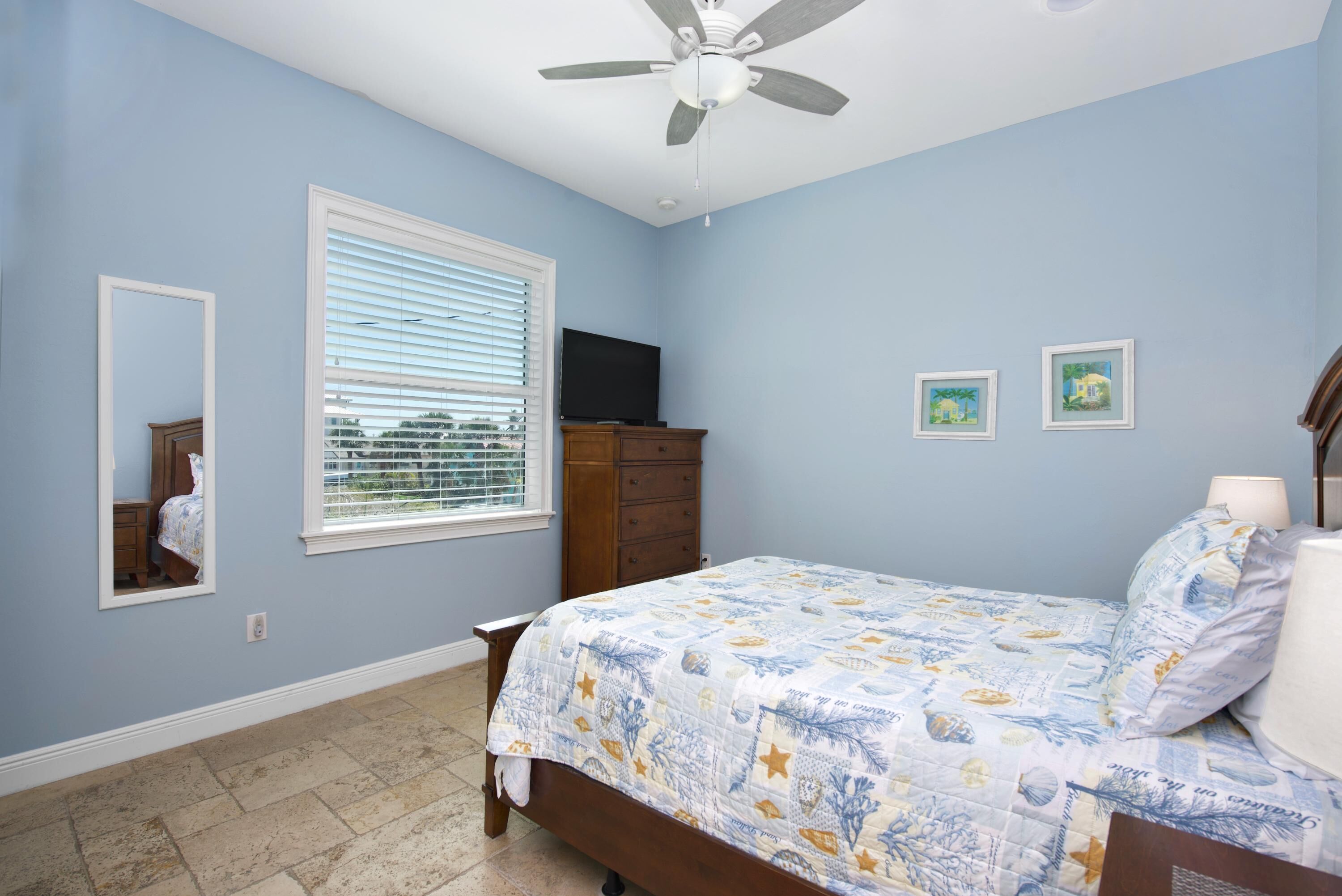 A bedroom with a bed, a dresser, a television, and a ceiling fan.