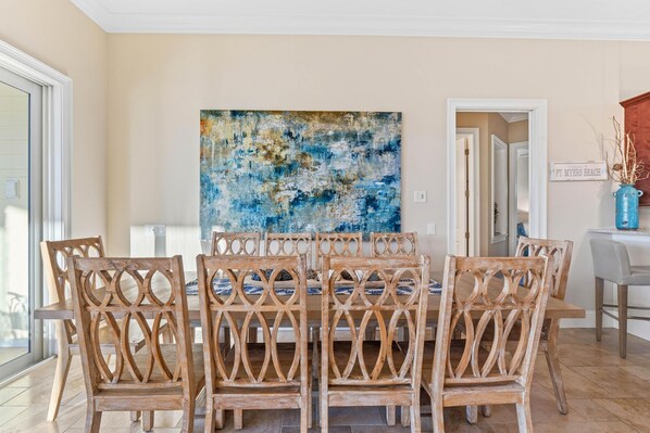 Un coin repas avec une table et des chaises en bois, un grand tableau abstrait accroché au mur et une pancarte sur laquelle on peut lire : « Bienvenue à Fort Myers Beach ».