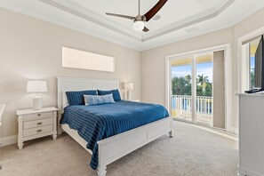 Une chambre dotée d’un grand lit, de deux tables de chevet, d’un ventilateur de plafond et offrant une vue sur l’extérieur grâce à une porte-fenêtre coulissante.