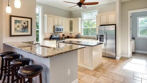 A kitchen with a central island, white cabinets, stainless steel appliances, and a ceiling fan. - Grande Palermo (Fort Myers Beach)