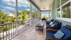 A covered balcony with wicker furniture, a table, and a view of lush greenery. - Grande Palermo (Fort Myers Beach)