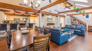 A spacious living area with a wooden dining table, blue sofas, and a staircase leading to an upper level. - Great Escape-5 (Fort Myers Beach)