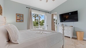 A bedroom with a bed, a TV, a dresser, and a balcony with a view of palm trees. - Sea La Vie (Fort Myers Beach)