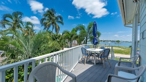 A deck with outdoor furniture, a railing, and a view of the water and palm trees. - Sea La Vie (Fort Myers Beach)