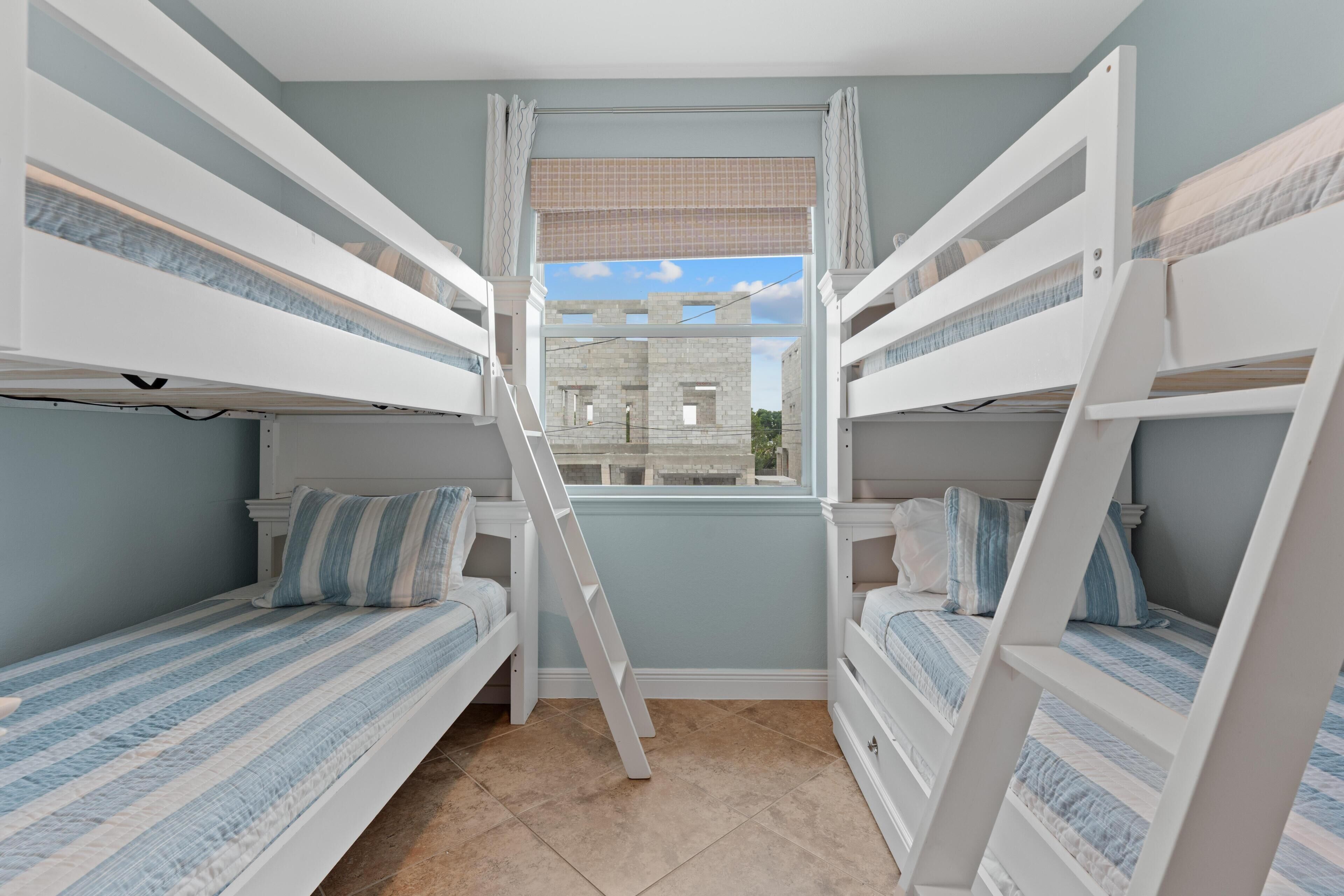 A room with bunk beds, a window with a view of a building, and a ladder.