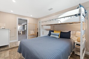 A bunk bed room with a desk and a chair, a bed with a patterned bedspread, and a view into an adjacent room. - Sandy Breeze (Fort Myers Beach)