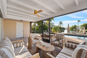 Una stanza luminosa con un'ampia finestra, una ventola a soffitto e vista su una piscina e palme.