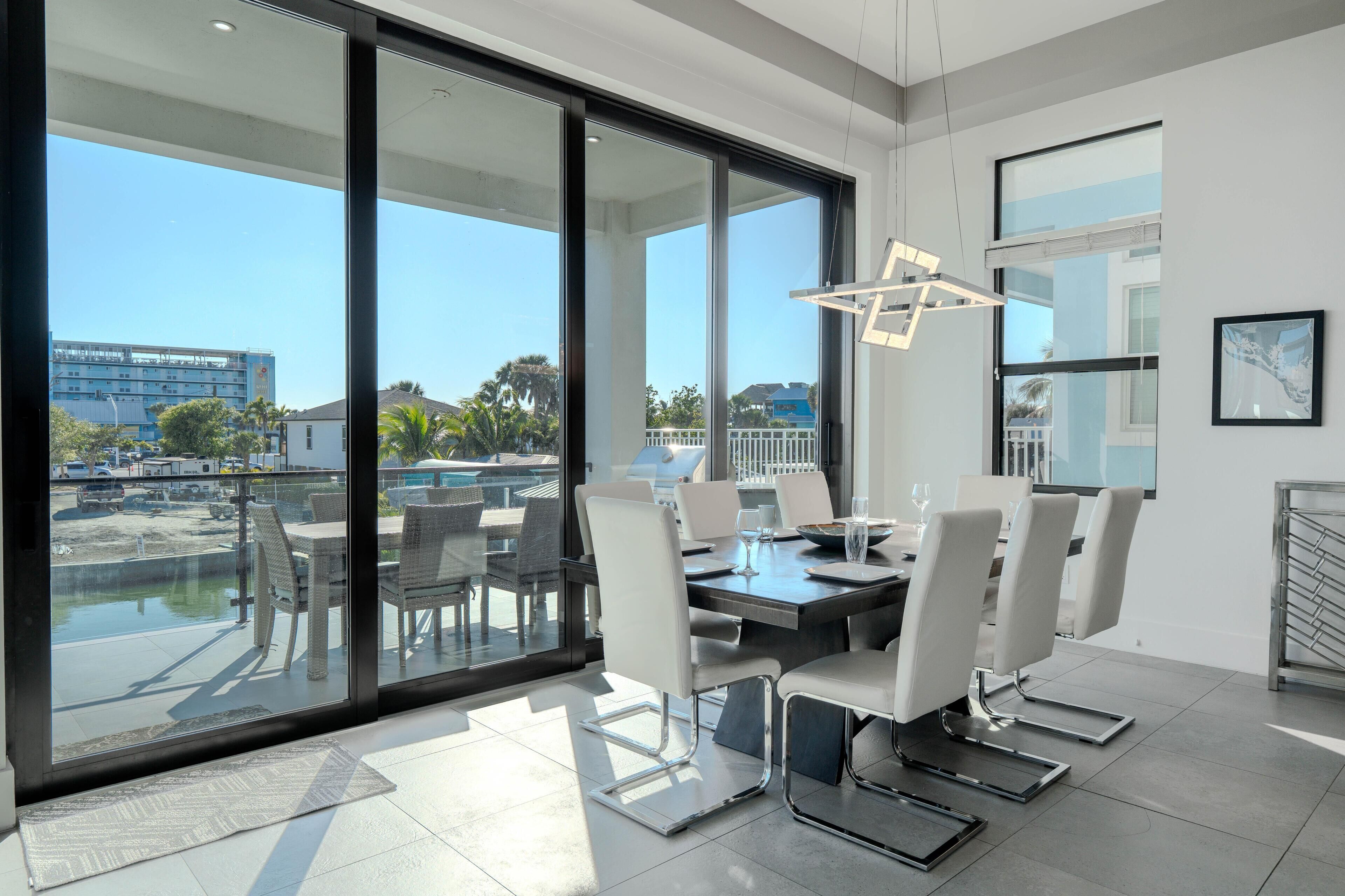 A modern dining area with a large glass window, a dining table with chairs, and a hanging light fixture.