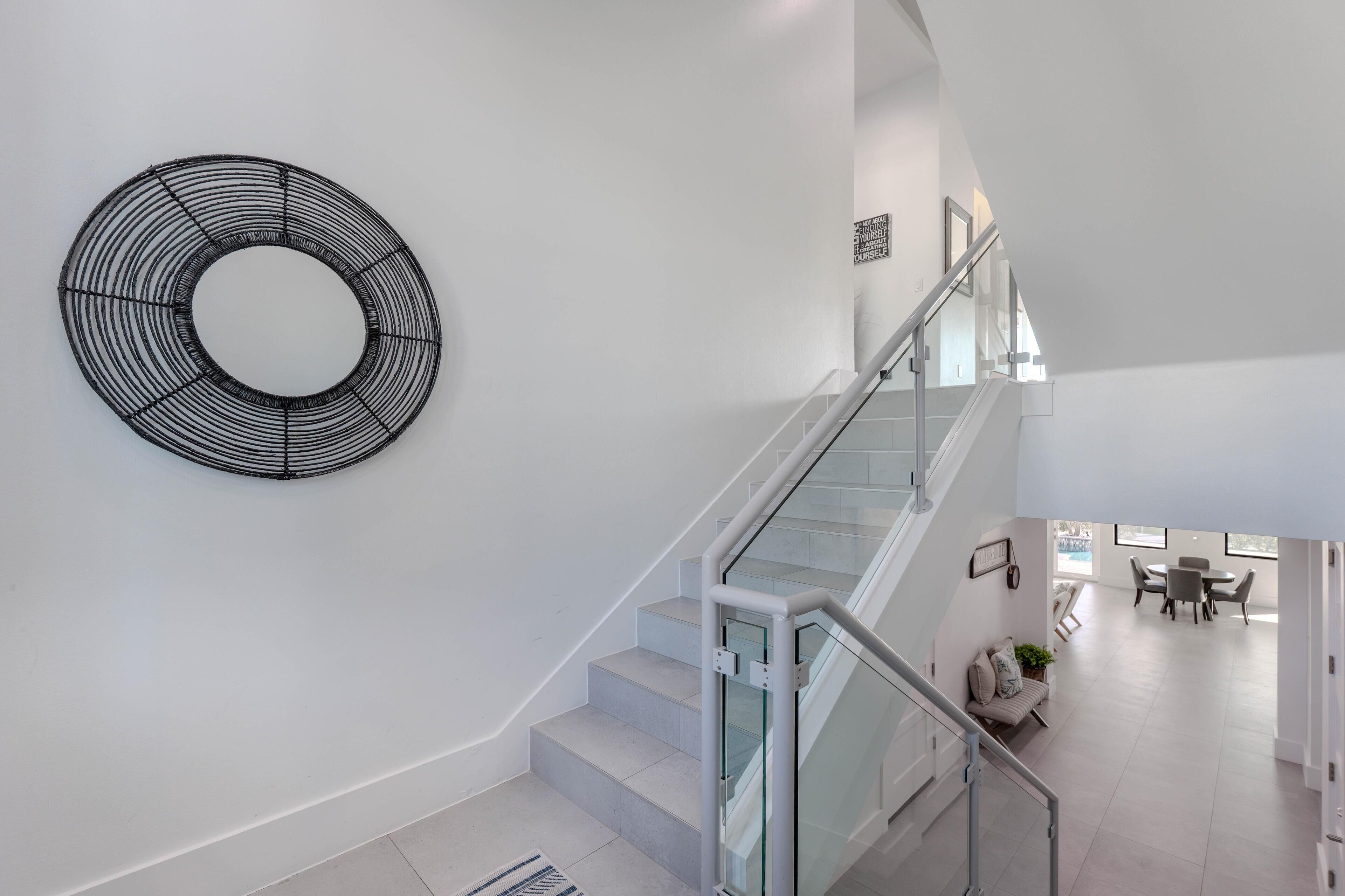 A modern interior with a staircase, a circular wall art piece, and a dining area with a view.