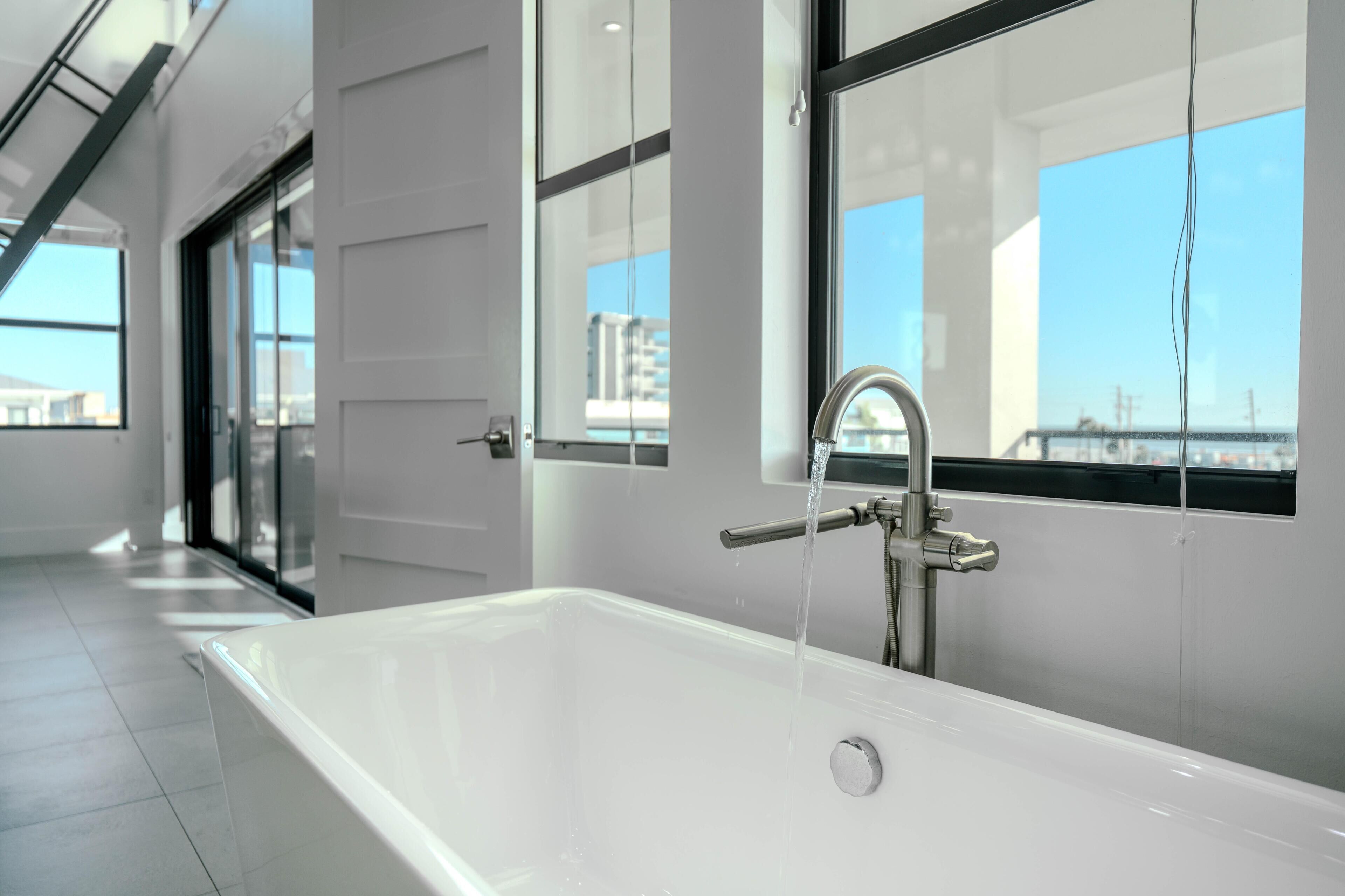 Un baño moderno con una bañera grande, cabina de ducha de vidrio y vistas a la ciudad a través de amplios ventanales.