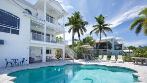 A two-story house with a swimming pool, outdoor furniture, and palm trees. - Dock Holiday (Fort Myers Beach)
