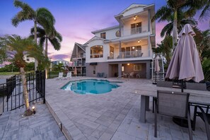 A two-story house with a swimming pool, outdoor furniture, and palm trees. - Dock Holiday (Fort Myers Beach)