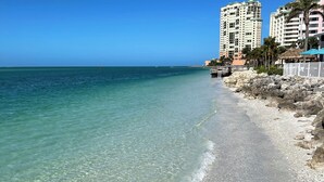 Una playa con agua turquesa cristalina, un litoral rocoso y edificios altos al fondo.