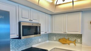 Una cocina con armarios blancos, un microondas de acero inoxidable, una placa de inducción negra y un salpicadero de azulejos.